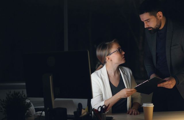 Two colleagues reviewing a document together in a dimly lit office at night — The Value Gap
